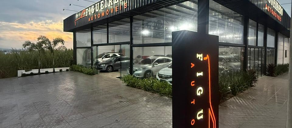 Fachada da Figueiredo Automóveis ao anoitecer, com o letreiro aceso